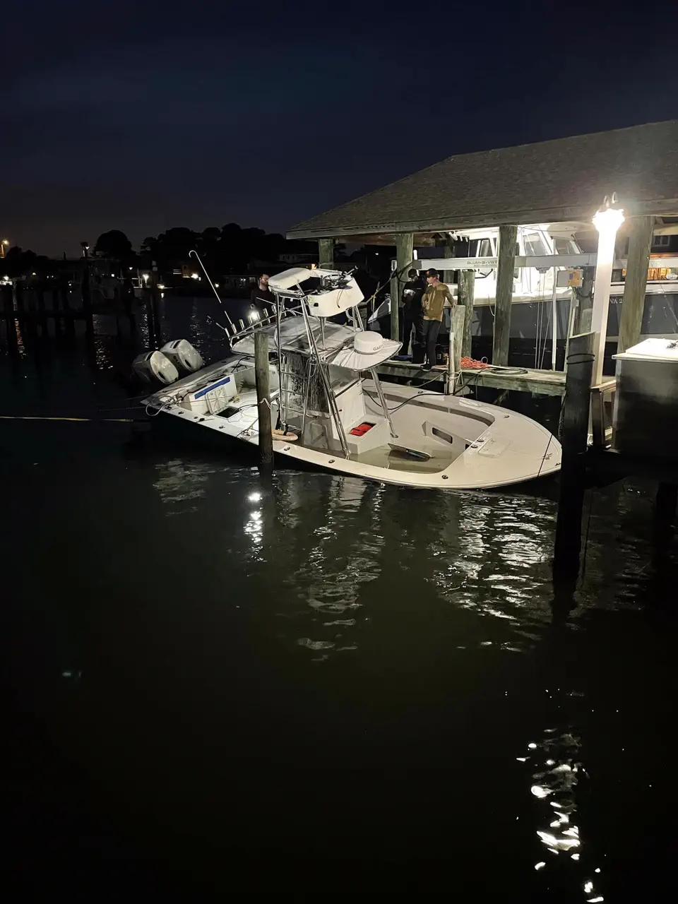 A recovered center-console boat afloat alongside a lit dock after dark