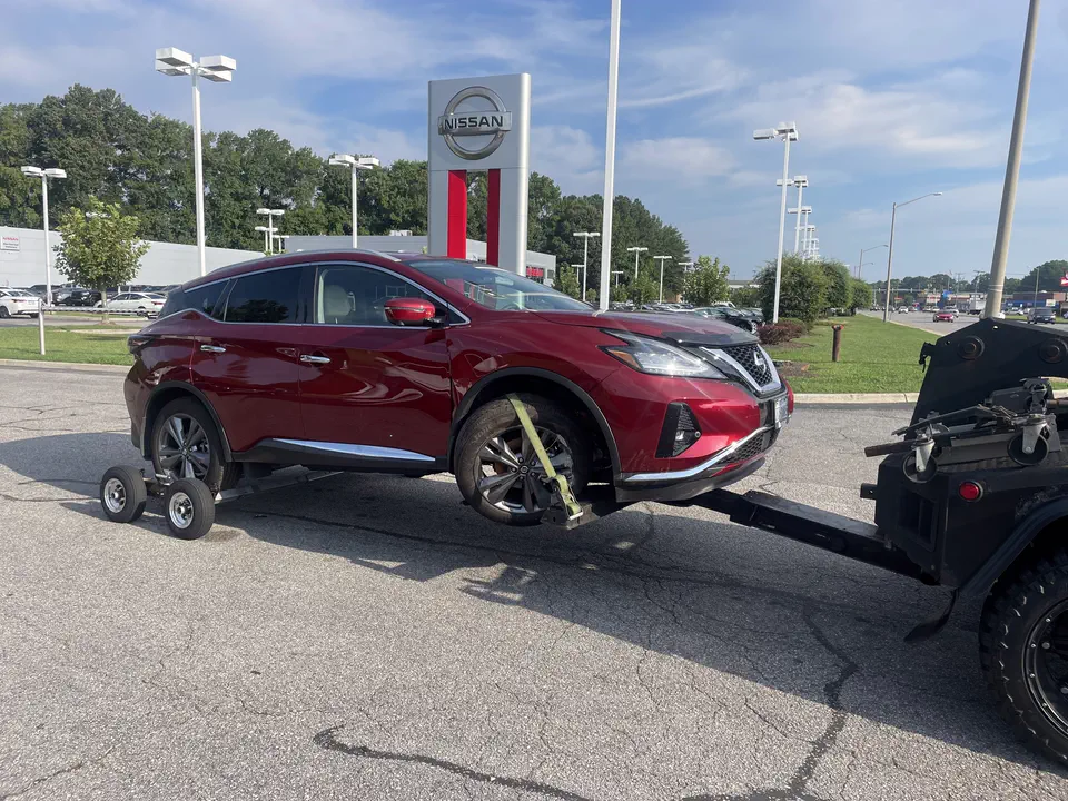 A red Nissan Murano strapped on the wheel-lift at a Nissan dealership